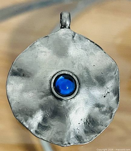 Handcrafted hammered metal pendant with a vibrant blue cabochon stone at its center. (1 of 2)