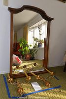 Full view of wood framed mirror with two brass wall sconces placed in front on green carpet.