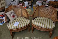 Pair of two wooden chairs with cane woven back and striped upholstered seat cushions photographed in a cluttered room.