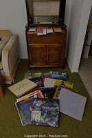 Full view of vintage Saba record player in wooden cabinet with vinyl records spread on the floor in front.