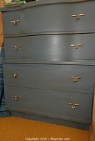 Front view of blue-gray painted wood dresser with four drawers and gold-tone wing-shaped handles.