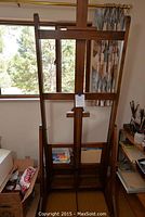 Full view of the wooden easel standing upright near a window with natural light. Easel shows vertical frame and adjustable support.