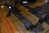 View of the glass top and intricately carved dark wood spindle legs and frame of the table.