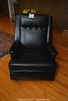 Front view of the black leather rocking recliner showing cushioned seat, back with button tufting, and padded arms.