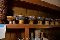 Seven decorative pottery bowls arranged on a shelf, showing variety in size and glaze color patterns.