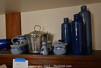 Shelf with three tall blue glass bottles marked 'James Poutman New York', several blue and white pottery items and a metal ice bucket.