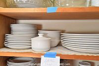Shelf showing grouped white ceramic dishes including plates, bowls, and a lidded container