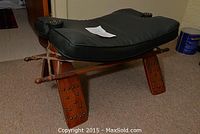 Front view of the wooden camel saddle seat showing black leather cushion and carved wooden legs with studs.