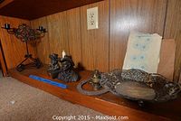 Wide view showing two Michael Garman statues, ornate pierced metal dish, brass burner, horseshoe and floral textile on wood shelf