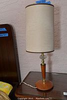 Full view of a vintage table lamp with beige cylindrical shade, wooden base, brass and glass details