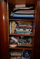 View of all fabric, yarn, and burlap bags stored on multiple shelves inside a wooden cabinet.