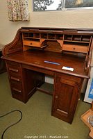 Full view of wooden roll top desk showing curved roll top, open work surface, upper compartments and drawers, bottom cabinet and drawers.