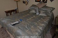 Full view of the queen bed made with sage green floral comforter, multiple pillows, and box spring underneath.