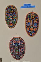 Three Huichol bead masks hanging on a wall, showing detailed colorful beadwork and traditional designs.