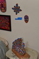 Three Huichol bead art pieces displayed: a beaded bird sculpture on a wooden base, two wall art pieces including a sun shape and a mask shape, all showcasing vibrant, colorful bead patterns.