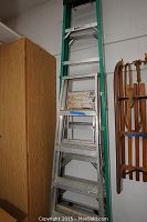 Two aluminum ladders: one green and silver multi-position ladder with black top cap and one silver stepladder with paint residue on steps and platform.