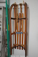 Full view of antique wooden sled with curved runners against a white wall, also showing a green ladder nearby.