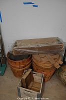 Photo showing large and smaller wooden fruit baskets stacked, with wooden yard tools on top wrapped in plastic.