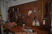 Wide view of pegboard with multiple hanging hand and garden tools and accessories on a workbench below.