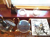 Two round glass side tables with brass legs and square glass pedestal table grouped beneath window