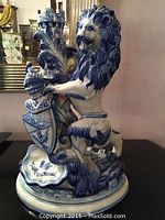 Full view of the blue and white glazed porcelain candlestick showing a rampant lion with a shield and castle turret behind on a scalloped base.