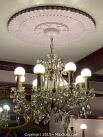 Overall view of eight-light crystal chandelier hanging from ceiling with bulbs illuminated