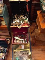 Three decorative boxes (black, red, gold) filled with assorted costume jewelry displayed on wood floor.