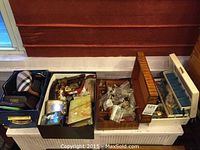 Four open boxes showing eyeglass cases in fabric and leather, decorative trinket boxes, black box with belt buckles and brooches, wooden box with jewelry