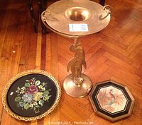 Photo showing solid brass stand with penguin figure base and the two decorative trays positioned around it on wood flooring.