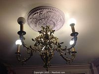 Frontal angled view of chandelier installed under ceiling medallion, showing scrollwork and five illuminated bulbs