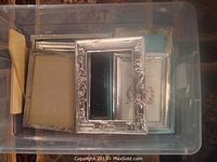 Overhead view of clear plastic bin containing nine sterling silver picture frames of various sizes and border designs
