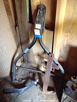 Tow bar with black metal frame and ball hitch, serial number visible, standing against a wooden wall with other tow accessories.