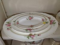 Three assorted platters with pink rose floral pattern and gold rims stacked on shelf