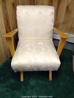 Front view of mid century armchair showing cream floral fabric upholstery and wooden armrests.