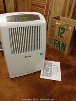 Amana dehumidifier with control panel and instruction manual on carpet, with fan box behind