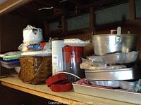 Kitchen shelf with various kitchen and baking items including storage containers, picnic basket, aluminum bowls, and baking pans.
