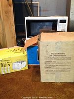 Image shows Daewoo microwave on a shelf behind boxed toaster and boxed ice cream freezer.