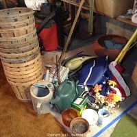 Photo showing stacked vegetable baskets, green plastic watering can, assorted small planters, ceramic pots, artificial flower wreath, and gardening tools.