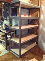 Full view of the shelving unit showing metal frame and five pressed wood shelves in a workshop environment.