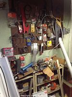 Assorted hand tools on pegboard and shelf, including hacksaw, tape measures, gloves, clamps, and boxes of torch kits