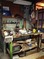 Photo of workbench surface with scattered tools, hardware, tool belts, nails, copper pipe and assorted wood pieces under the table.
