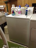 Front and side view of white Kenmore 80 Series top load washer with detergent and cleaning products placed on top.