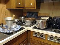 Multiple kitchen cookware and utensils on a kitchen counter including metal pans and a large aluminum sieve.