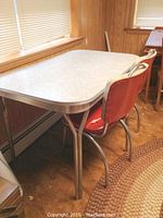 Dining table with chrome edging, chrome legs and laminate patterned top, with two matching chrome framed red vinyl chairs.