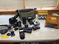 Wide view showing Minolta X700 camera body with lenses, flashes, accessories, and camera bag on table.
