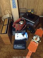 Overview of lot showing camera, car phone case, joysticks, Mickey Mouse clock watch on orange leather strap, and large box likely a typewriter box