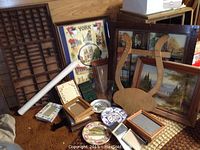 Various wall art, frames, decorative plates, and a large wooden type case on floor against wall