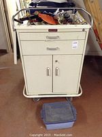 Front view of the cream-colored Harloff metal cabinet on wheels with various tools and hardware on top and in drawers.