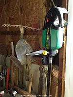 Photo showing metal garden tools with wooden handles, and WeedEater TapN'Go cordless trimmer mounted on wall