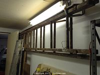 Long wooden extension ladder hanging horizontally on wall, showing weathered wood with paint and signs of frequent use.